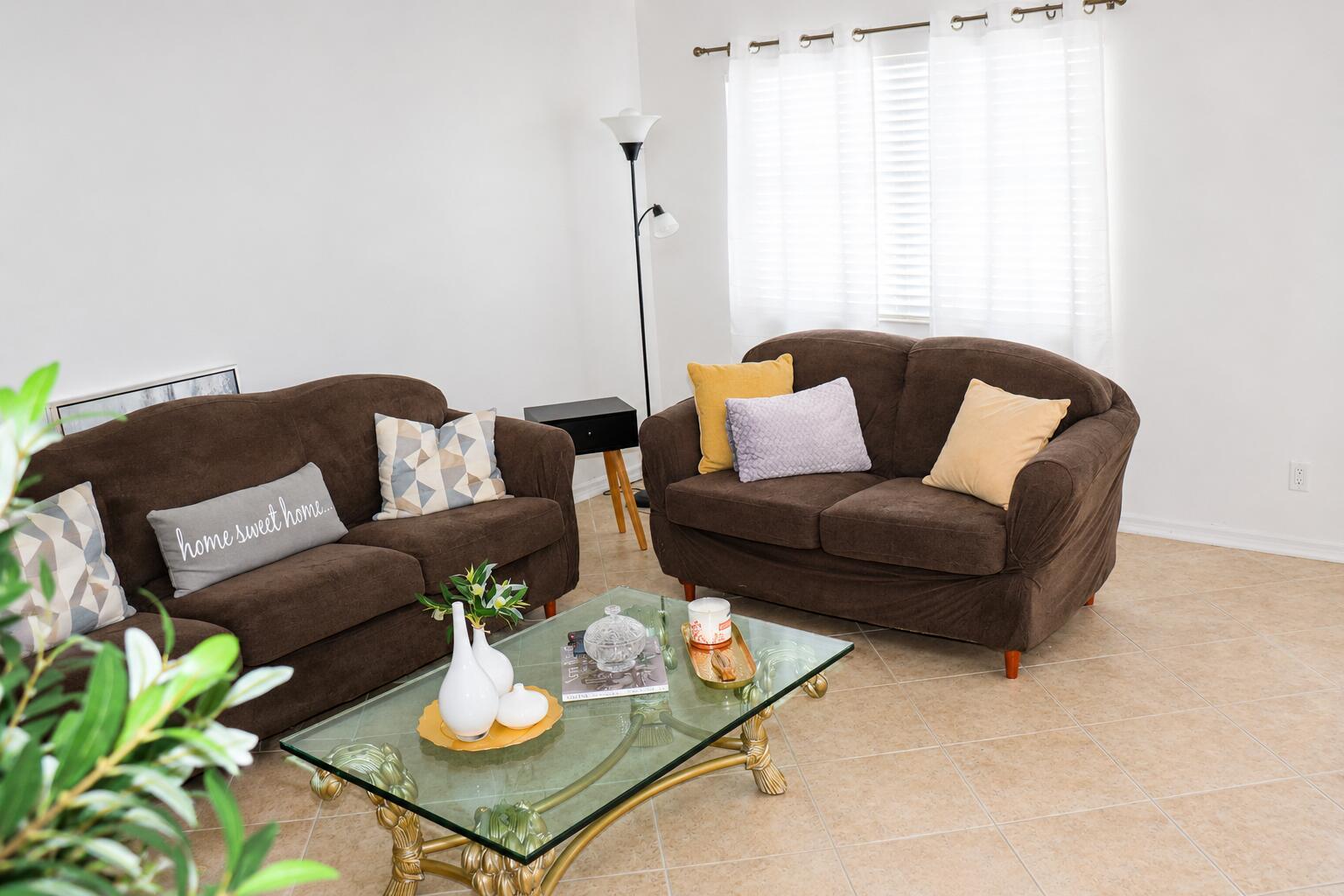 A living room features two brown sofas, a glass coffee table, and tile flooring — 148 Tuscany # B, Delray Beach FL 33446, DELRAY BEACH, FL