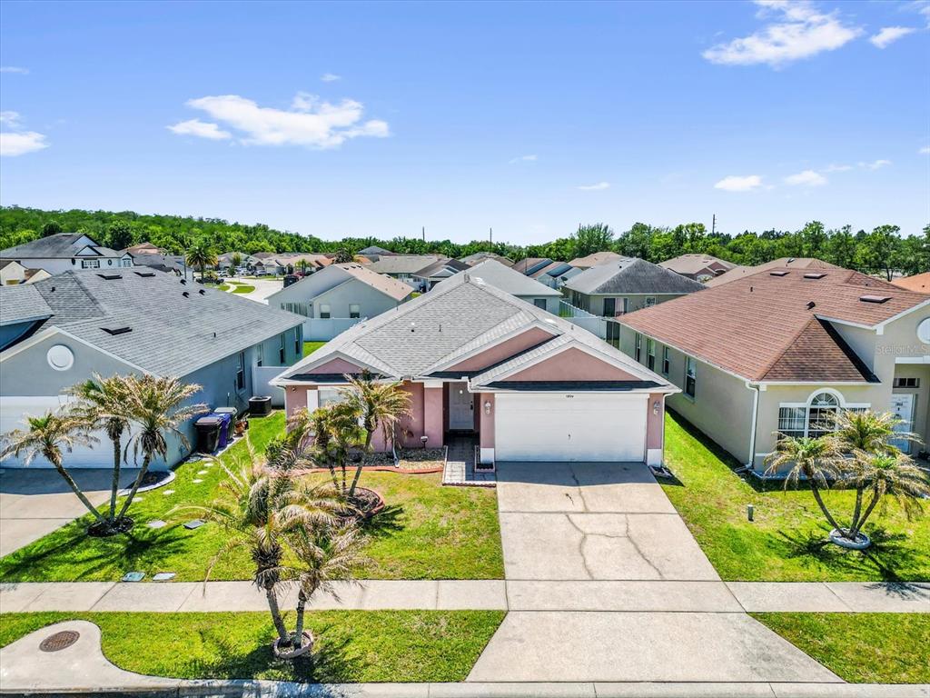 An exterior view of a single-story suburban house with a two-car garage and palm trees — 1804 BAGUETTE COURT, KISSIMMEE, FL