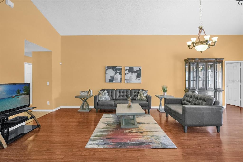 A living room features dark gray sofas, a patterned area rug, and light orange walls — 1804 BAGUETTE COURT, KISSIMMEE, FL