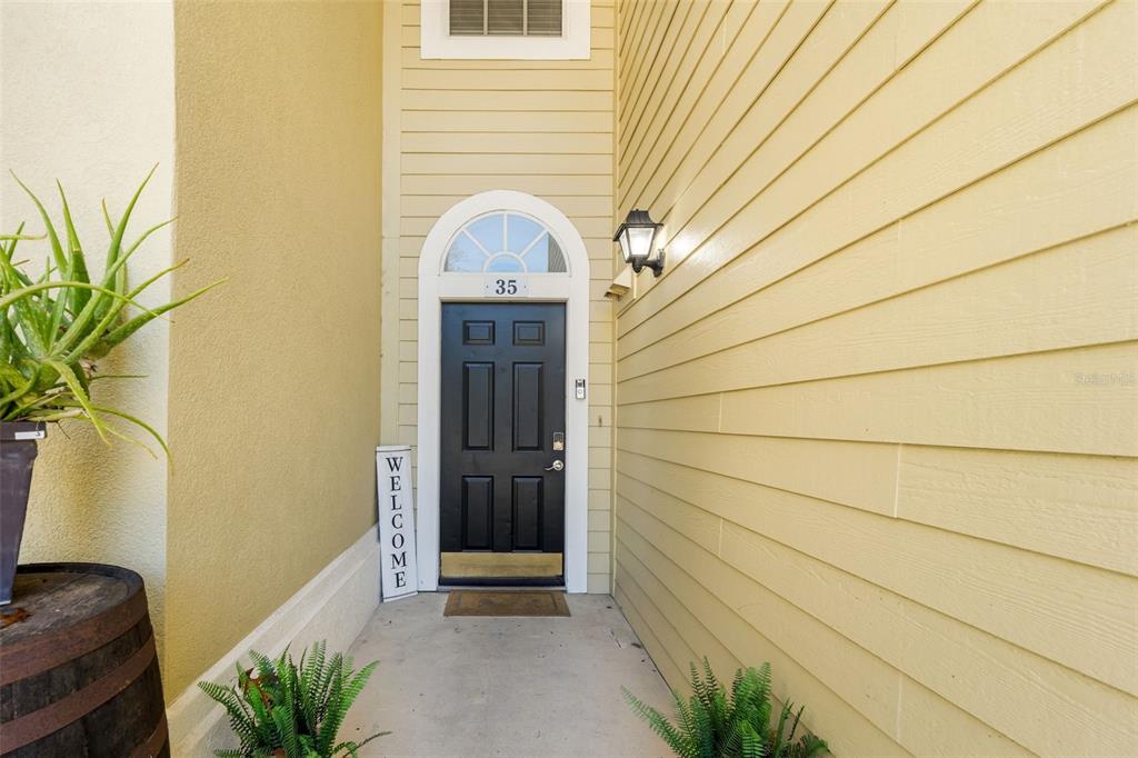 A black front door with a transom window sits under a light fixture on a porch — 10000 SW 52ND AVENUE UNIT 35, GAINESVILLE, FL