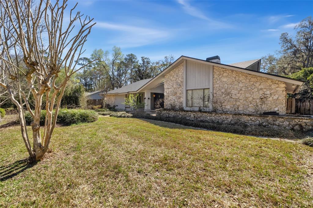 A single-story house features a stone facade, a gabled roof, and a large front lawn — 2345 NW 14TH PLACE, GAINESVILLE, FL