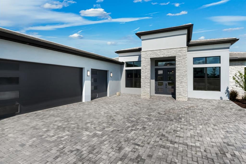A modern single-story house exterior with a stone-accented entryway, dark garage doors, and paver driveway — 2428 WATERFRONT CIRCLE, SARASOTA, FL