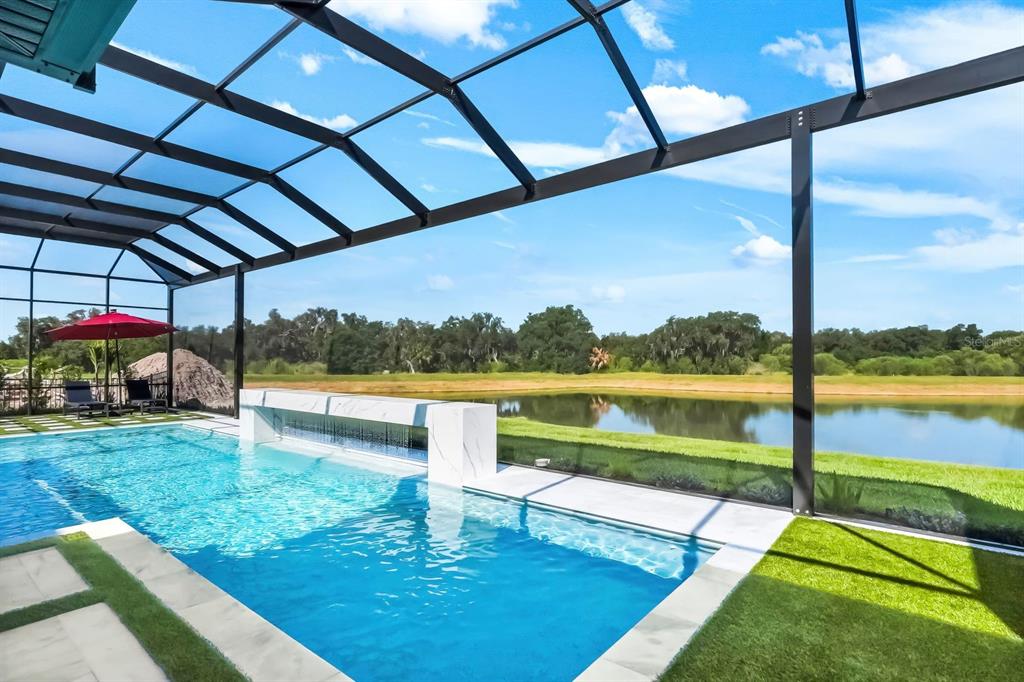 A swimming pool with a water feature overlooks a pond from a screened-in patio — 2428 WATERFRONT CIRCLE, SARASOTA, FL