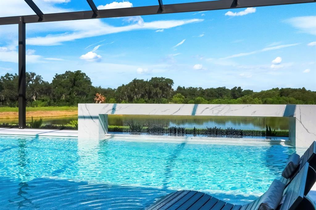 A swimming pool with a marble-clad water feature overlooks a lake and wooded landscape — 2428 WATERFRONT CIRCLE, SARASOTA, FL