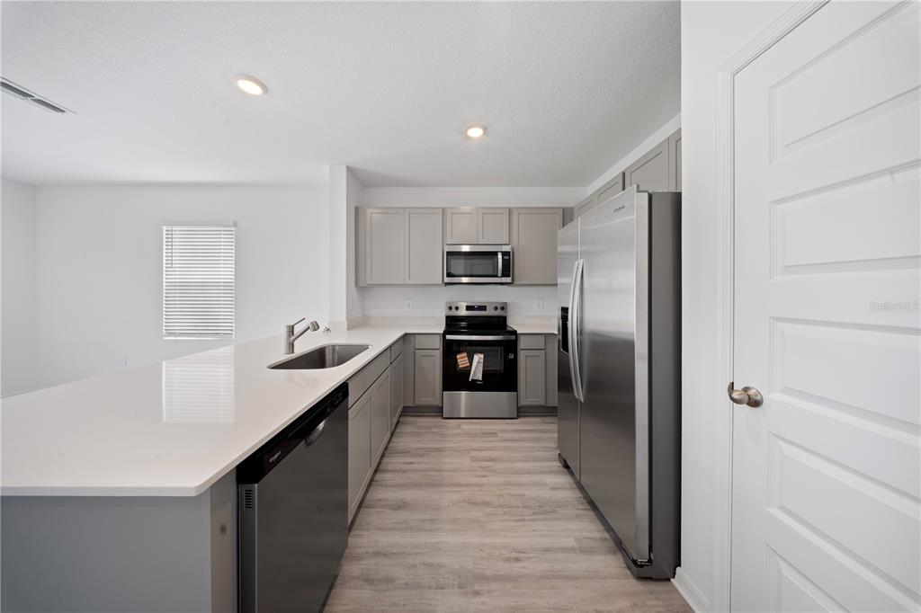A modern kitchen features gray cabinets, stainless steel appliances, and a white quartz island countertop — 4302 BUTTERSCOTCH CIRCLE, LAKELAND, FL