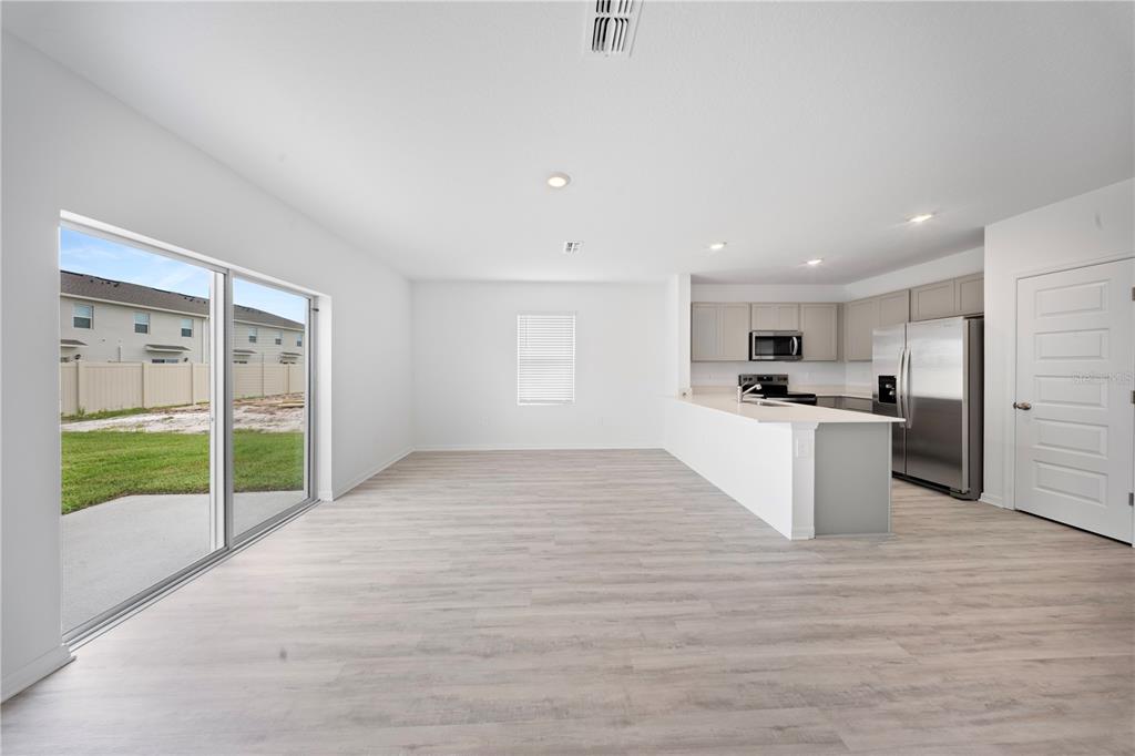 An open-concept living area with light wood-look flooring, a kitchen island, and sliding glass doors — 4302 BUTTERSCOTCH CIRCLE, LAKELAND, FL
