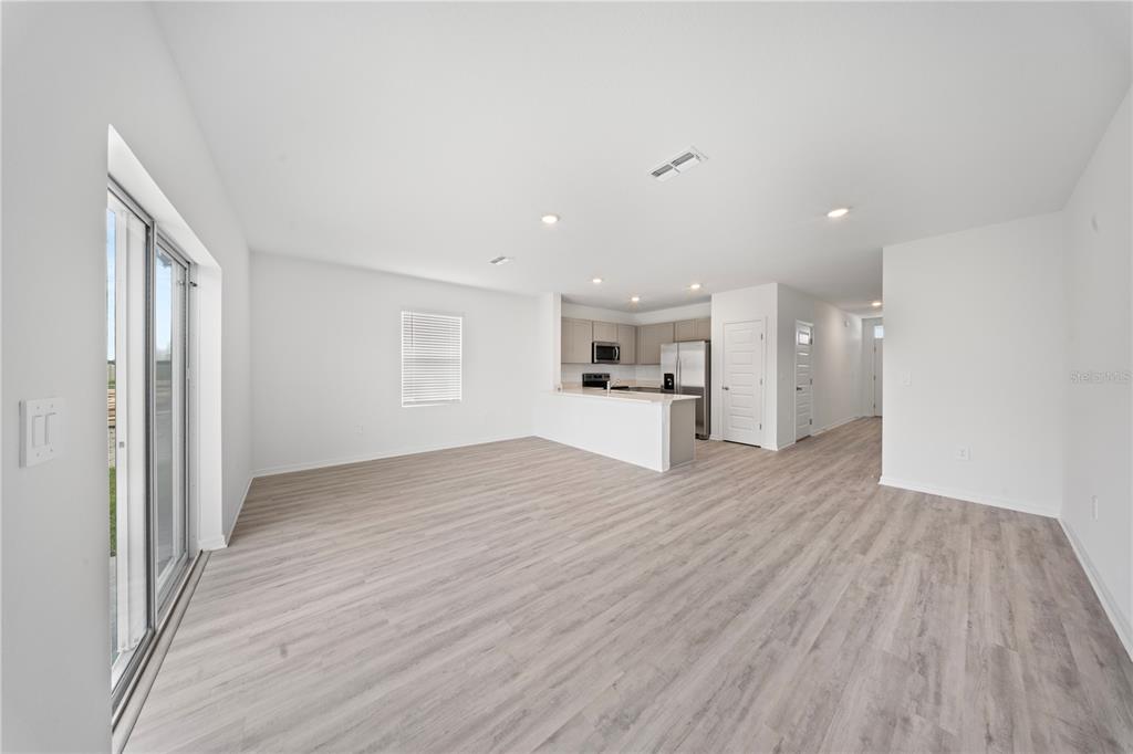 An open-concept living area features light wood-look flooring, white walls, and a kitchen with stainless appliances — 4302 BUTTERSCOTCH CIRCLE, LAKELAND, FL