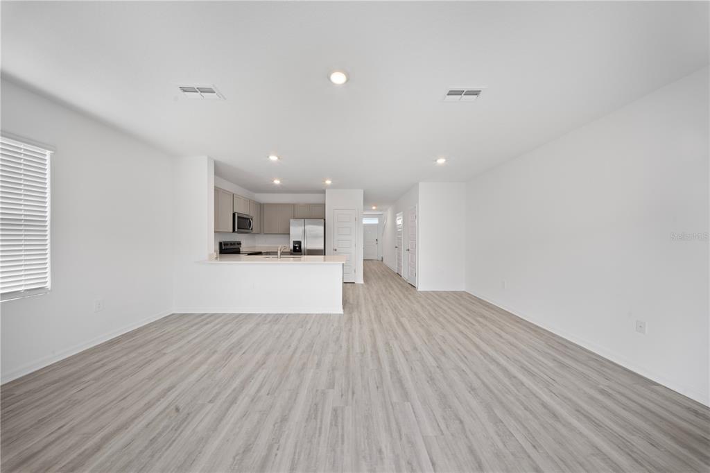 An open-concept living area features light wood-look flooring, white walls, and a kitchen with cabinets — 4302 BUTTERSCOTCH CIRCLE, LAKELAND, FL