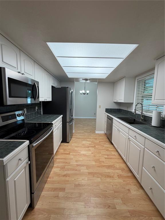 A galley kitchen features white cabinets, dark countertops, stainless steel appliances, and a large skylight — 3727 DUNWICH AVENUE, ORLANDO, FL