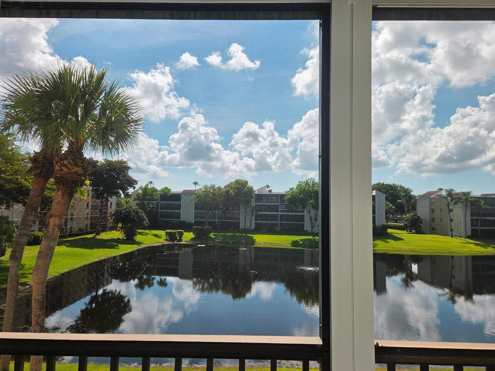 A view of a pond and apartment buildings from a screened-in balcony — 14310 Strathmore Lane # 305, Delray Beach FL 33446, DELRAY BEACH, FL