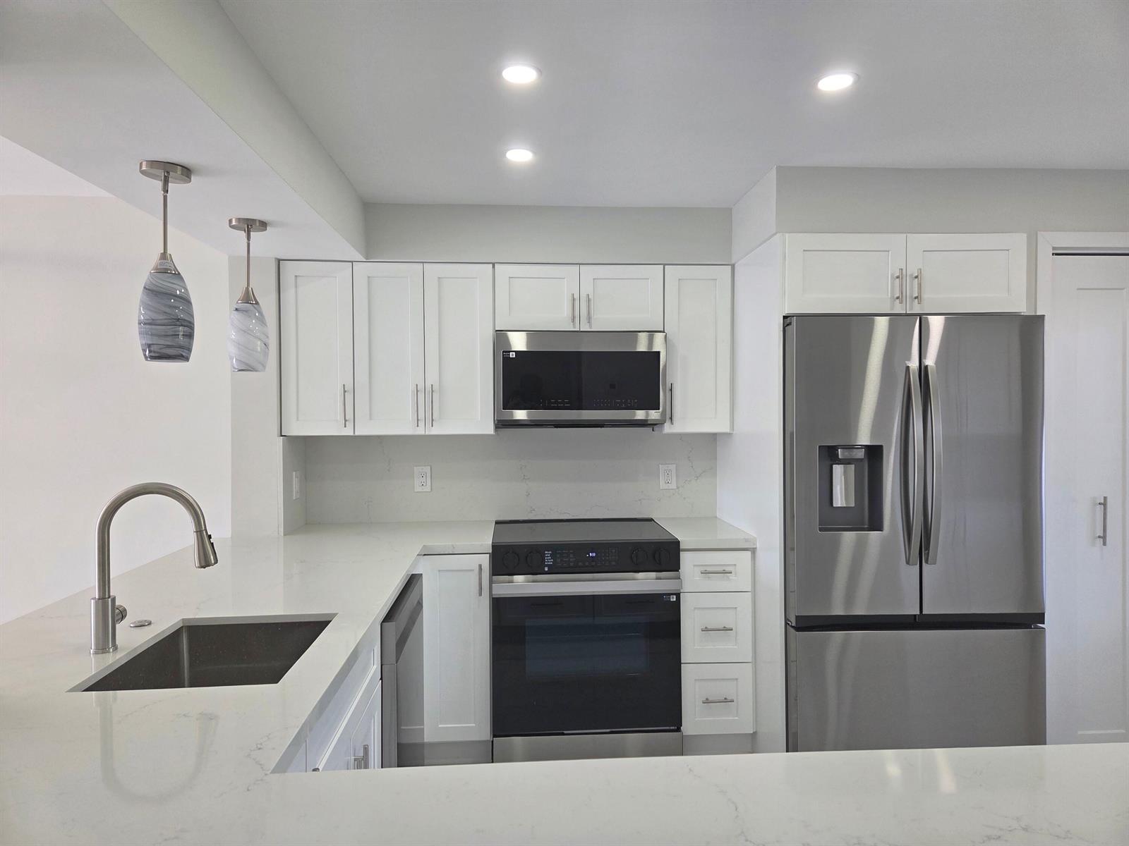 A modern kitchen features white cabinetry, stainless steel appliances, and white quartz countertops — 14310 Strathmore Lane # 305, Delray Beach FL 33446, DELRAY BEACH, FL