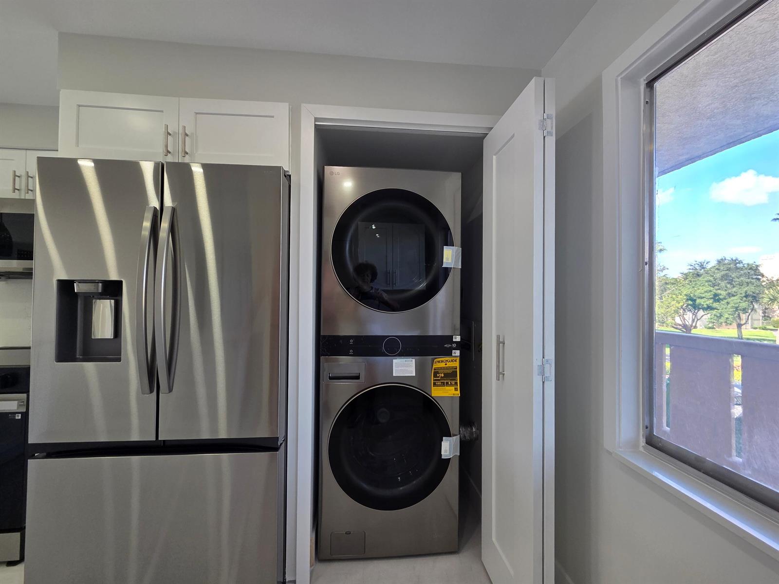 A stainless steel stacked washer and dryer unit sits in a closet next to a refrigerator — 14310 Strathmore Lane # 305, Delray Beach FL 33446, DELRAY BEACH, FL