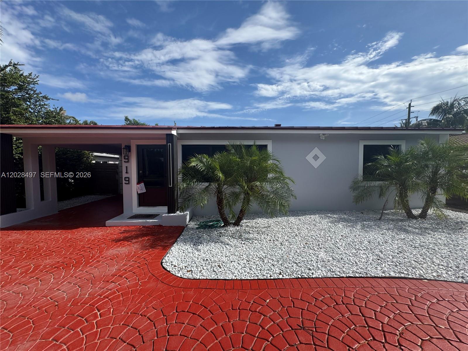 A single-story house features a red stamped concrete driveway, a carport, and an American flag — 919 NE 4th Ct, Hallandale Beach FL 33009, HALLANDALE BEACH, FL
