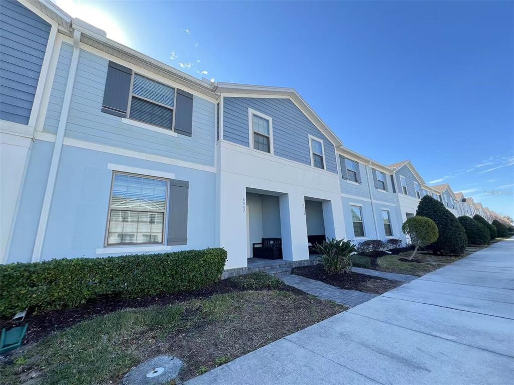 A row of light blue townhouses with white trim and a sidewalk in the foreground — 8942 SYDNEY AVENUE, KISSIMMEE, FL