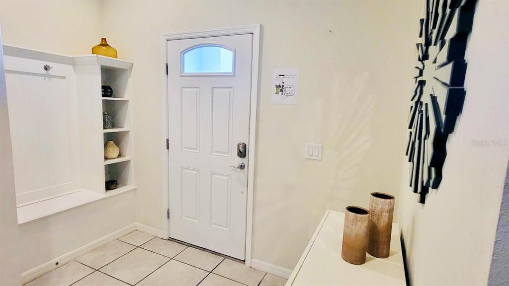 An entryway features a white front door, a built-in bench with shelving, and tile flooring — 8942 SYDNEY AVENUE, KISSIMMEE, FL