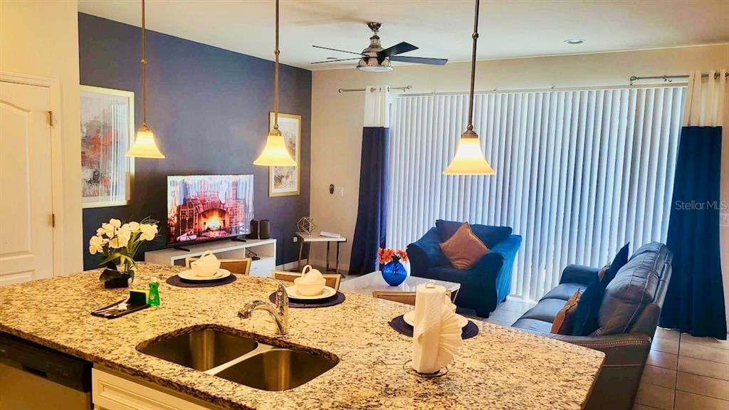A kitchen island with a granite countertop overlooks a living room with blue accent walls — 8942 SYDNEY AVENUE, KISSIMMEE, FL