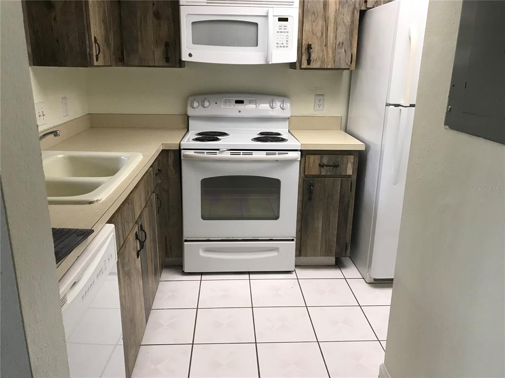 A kitchen features white appliances, wood-look cabinets, beige countertops, and white tiled flooring — 13610 S VILLAGE DRIVE UNIT 4103, TAMPA, FL
