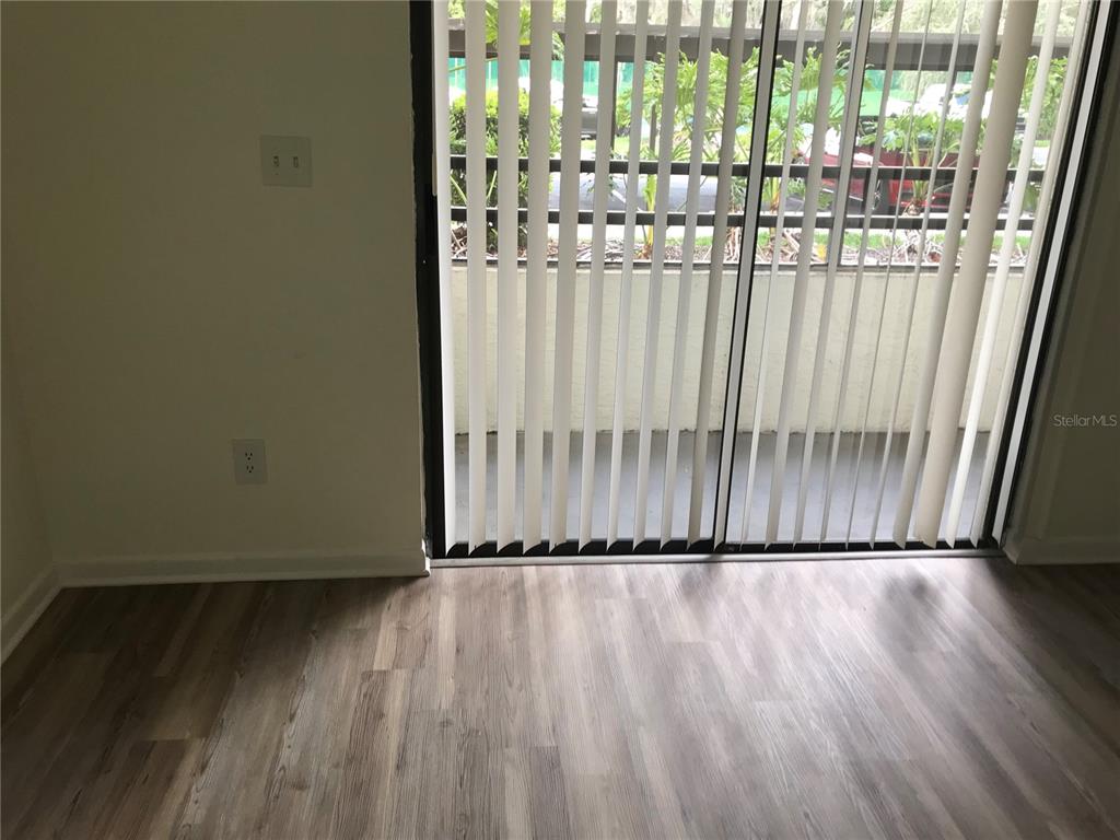 An interior room with wood-look flooring and vertical blinds covering a sliding glass door — 13610 S VILLAGE DRIVE UNIT 4103, TAMPA, FL