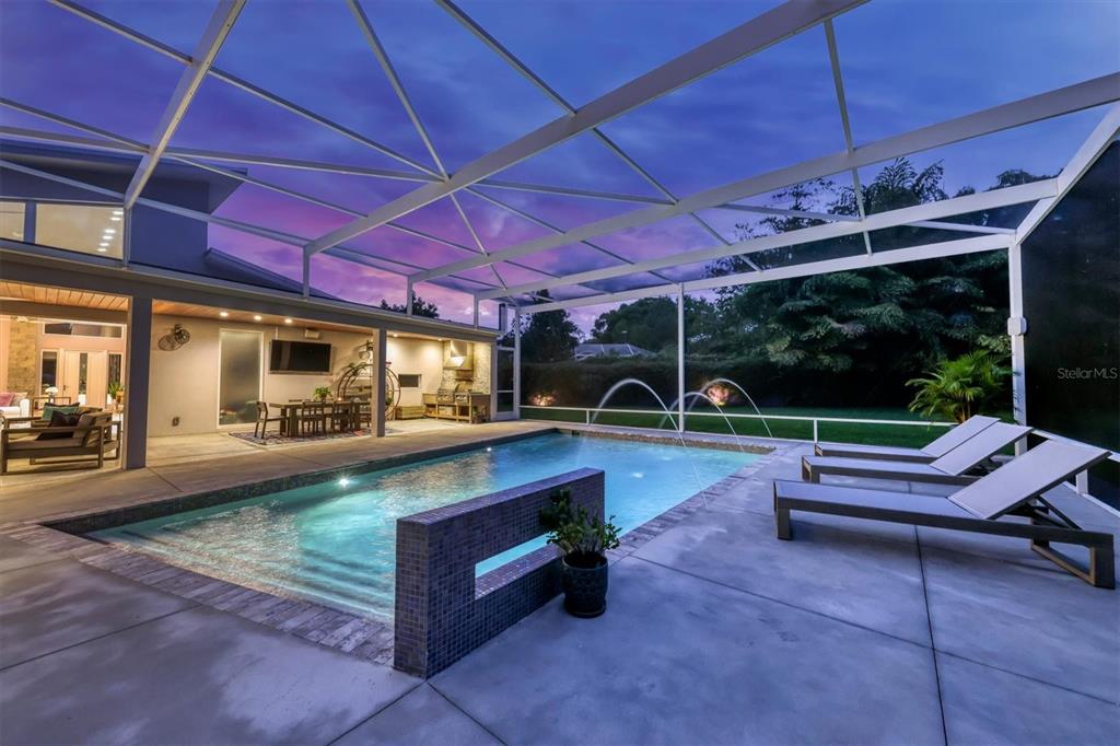 A screened-in patio features a swimming pool with water fountains and an outdoor kitchen area — 1556 EASTBROOK DRIVE, SARASOTA, FL