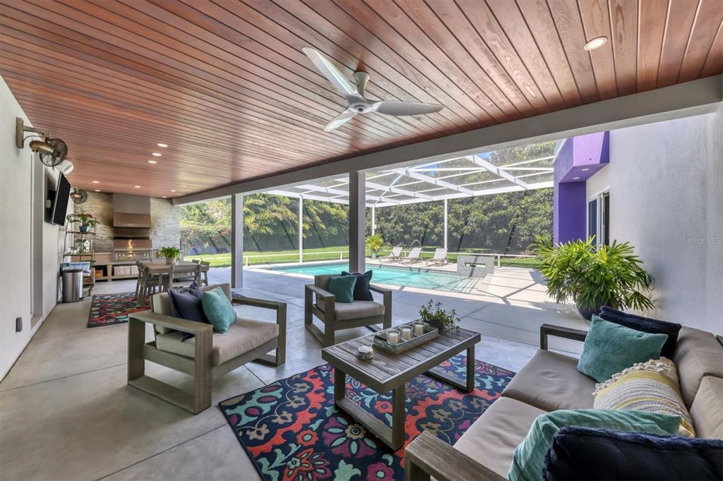 A covered outdoor patio features a wood-paneled ceiling, seating area, and a view of a pool — 1556 EASTBROOK DRIVE, SARASOTA, FL