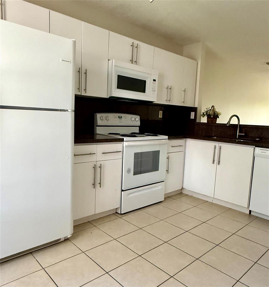 A kitchen features white cabinets, white appliances, dark countertops, and light-colored tile flooring — 3142 SW 129th Way # 156, Miramar FL 33027, MIRAMAR, FL