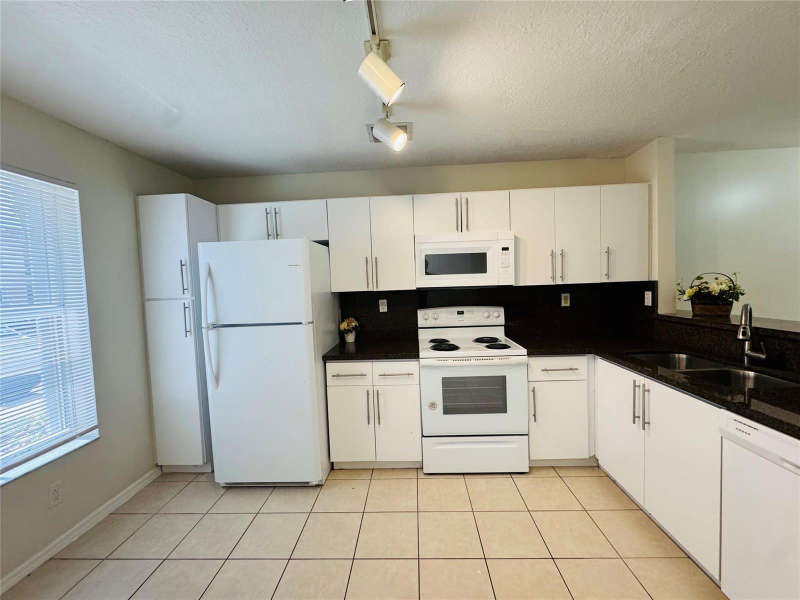 A kitchen features white cabinets, white appliances, dark countertops, and light-colored tile flooring — 3142 SW 129th Way # 156, Miramar FL 33027, MIRAMAR, FL