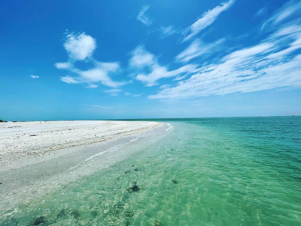 A sandy beach meets clear turquoise water under a bright blue sky with scattered clouds — 7140 FANCY STREET, ENGLEWOOD, FL