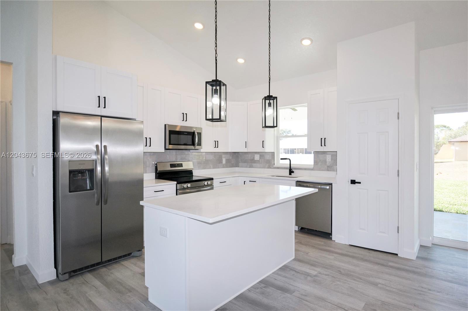 A modern kitchen features white cabinets, stainless steel appliances, a center island, and gray flooring — 3915 EL RADO AVE, Sebring FL 33872, SEBRING, FL
