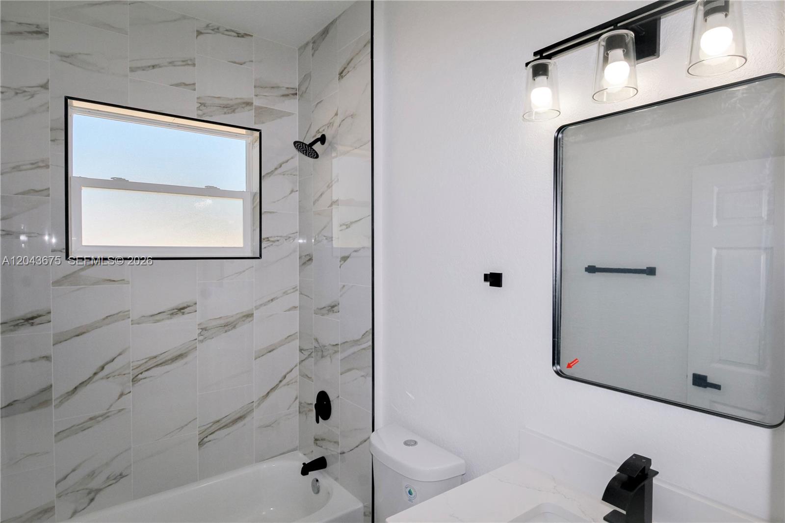 A bathroom features a marble-tiled shower, a white vanity, and a black-framed mirror — 3915 EL RADO AVE, Sebring FL 33872, SEBRING, FL