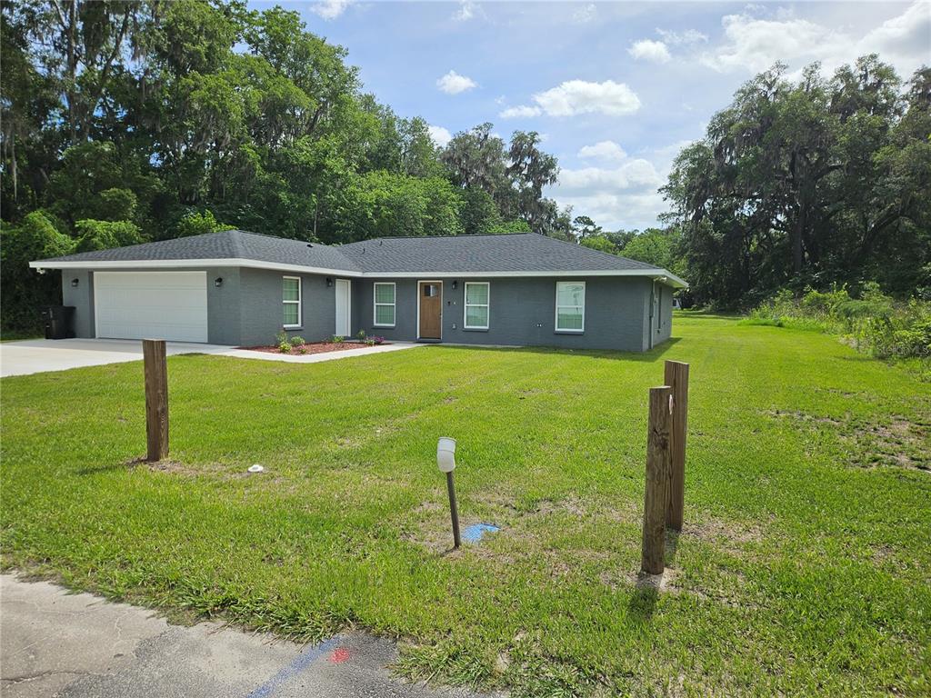 A gray, single-story ranch-style house with a two-car garage sits on a grassy lot — 51 NE 10TH STREET, WILLISTON, FL