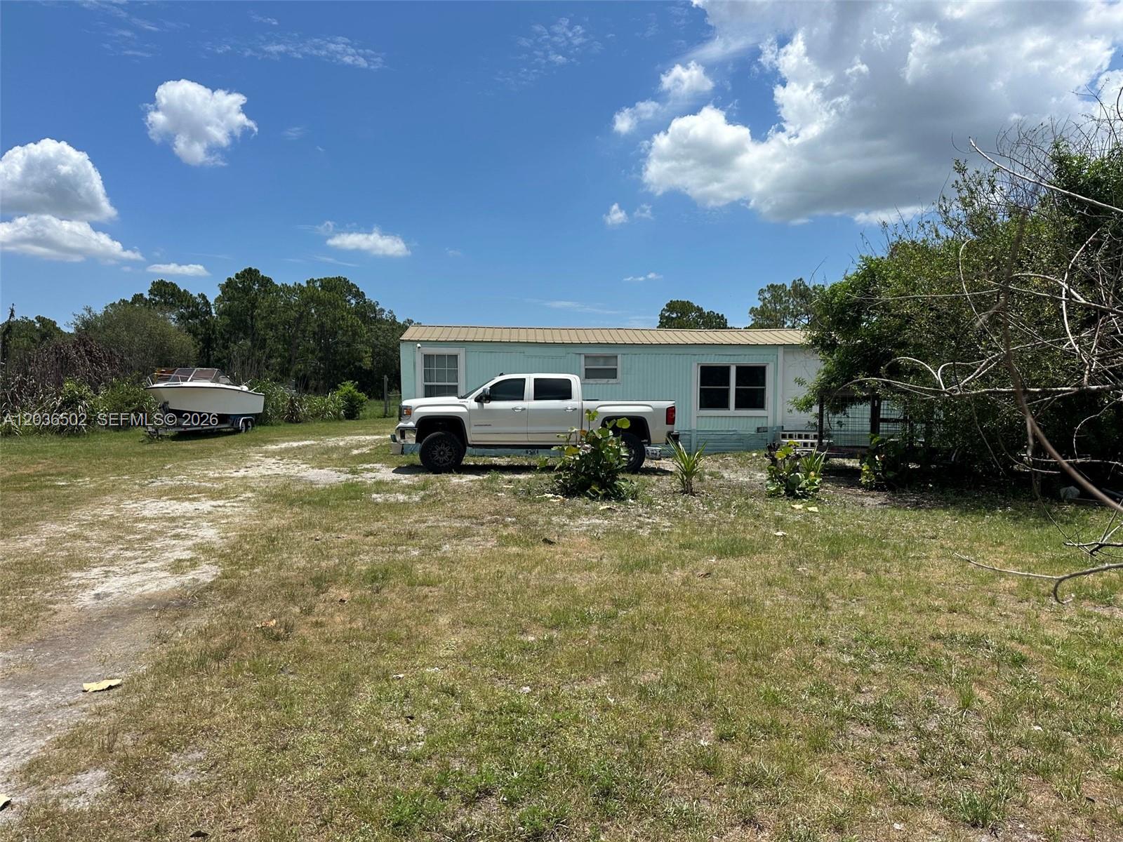 A light blue mobile home sits on a grassy lot with a white pickup truck parked — 135 S Hacienda, Clewiston FL 33440, CLEWISTON, FL