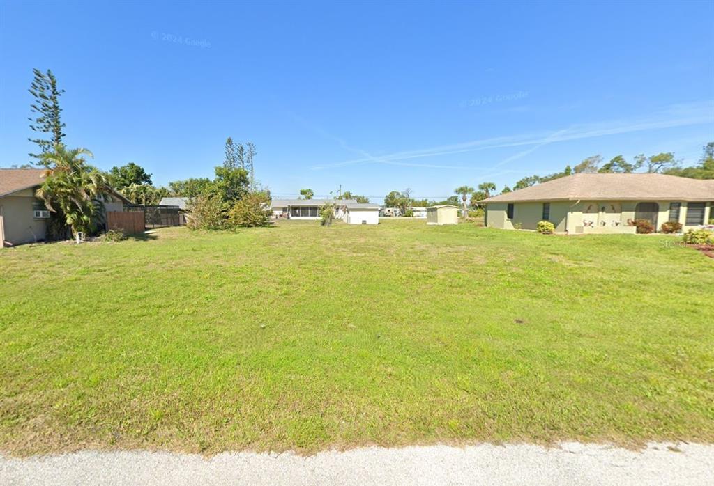 A paved road runs alongside a large, grassy vacant lot with houses in the background — 1274 CORAL LANE, ENGLEWOOD, FL