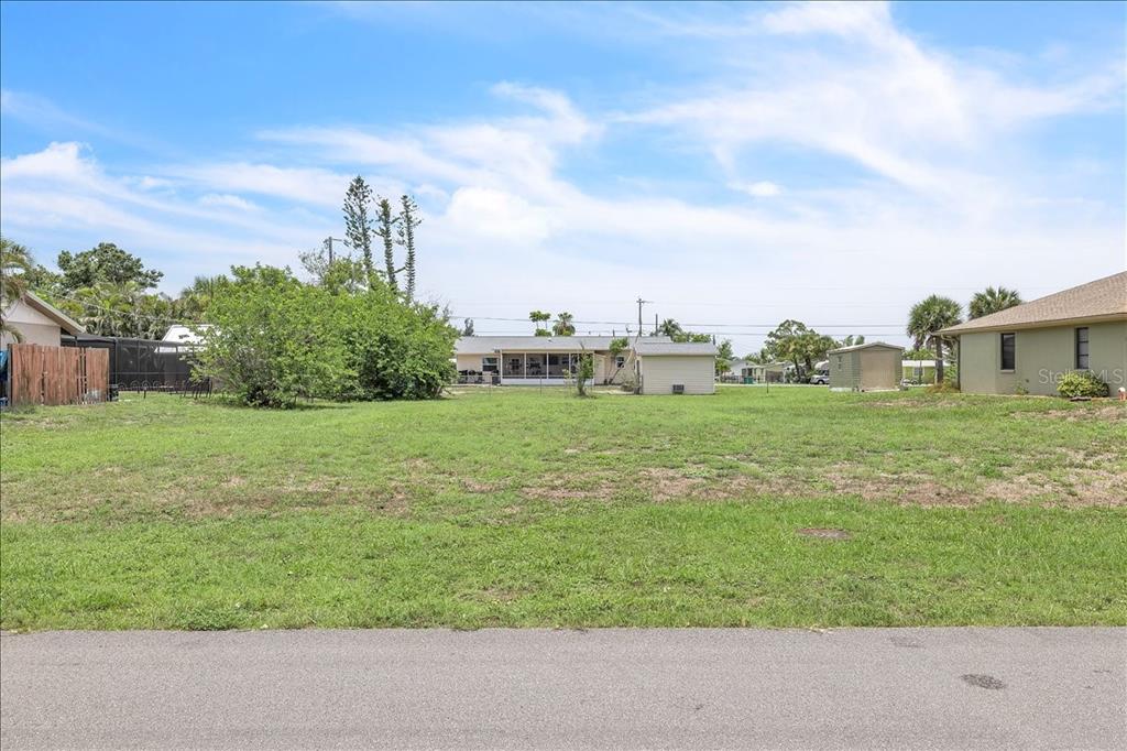 A grassy vacant lot sits between two houses under a blue sky with clouds — 1274 CORAL LANE, ENGLEWOOD, FL