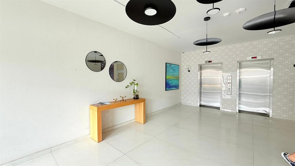 A modern lobby features a wooden console table, two circular mirrors, and two stainless elevators — 37 ISLA VERDE AVE. UNIT 203, CAROLINA, PR