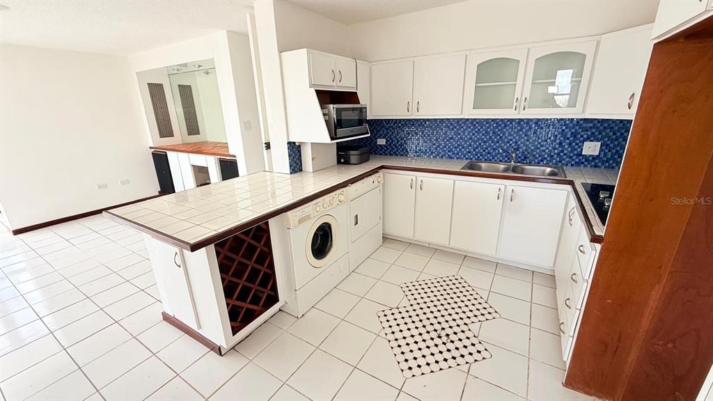 A kitchen features white cabinets, tiled countertops, a blue mosaic backsplash, and a built-in washer — 37 ISLA VERDE AVE. UNIT 203, CAROLINA, PR