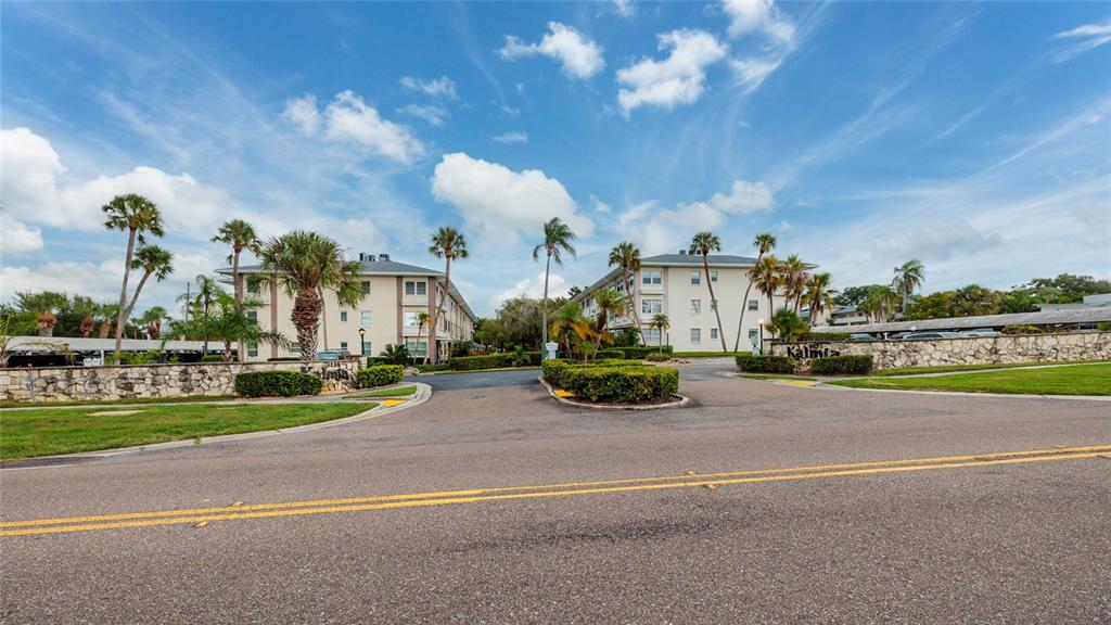 A view of two multi-story apartment buildings with palm trees and a stone wall entrance — 1235 S HIGHLAND AVENUE UNIT 2-301, CLEARWATER, FL