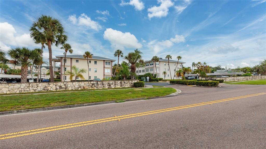 A street view of a multi-story apartment complex with palm trees and a stone wall — 1235 S HIGHLAND AVENUE UNIT 2-301, CLEARWATER, FL