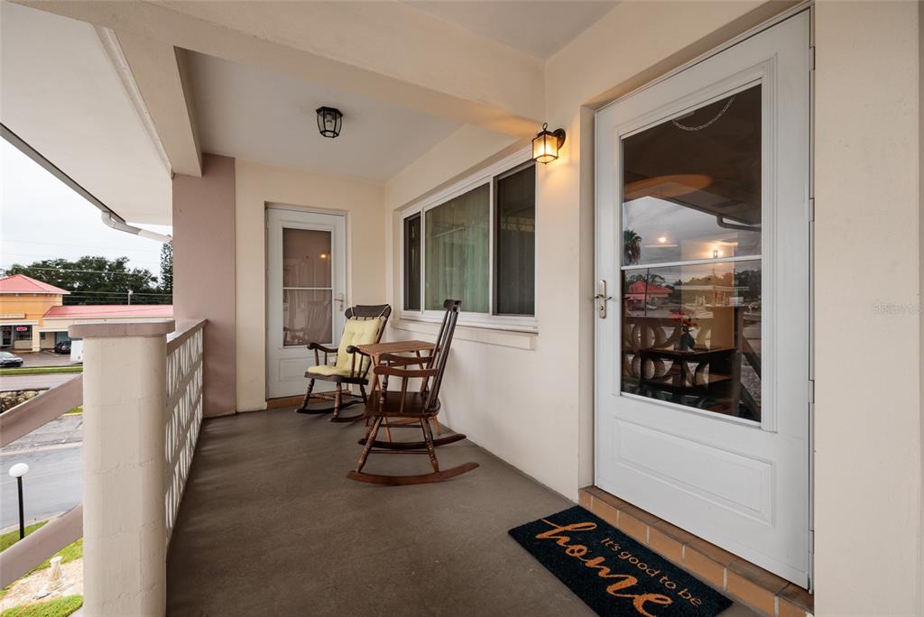 A covered porch features two wooden rocking chairs, a small table, and a front door — 1235 S HIGHLAND AVENUE UNIT 2-301, CLEARWATER, FL