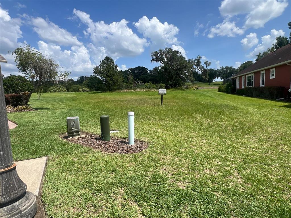 A vacant grassy lot features utility boxes and a real estate sign next to a house — 19492 FOREST GARDEN COURT, BROOKSVILLE, FL