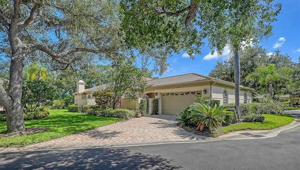 A single-story house with a beige exterior, tiled roof, and a paved driveway under trees — 3331 HADFIELD GREENE UNIT 49, SARASOTA, FL