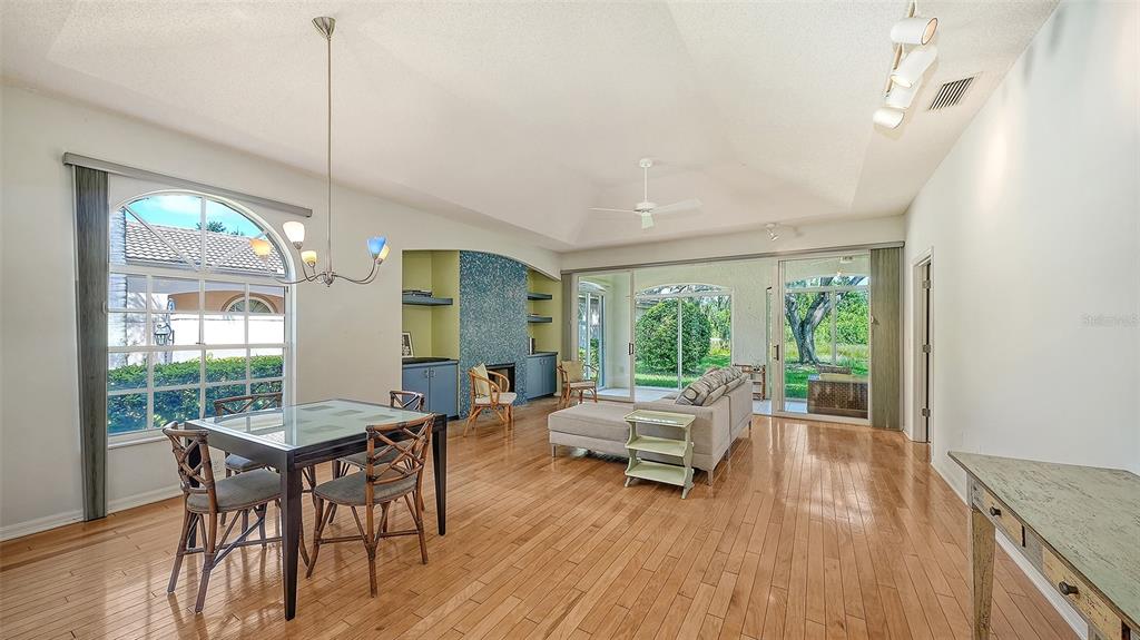 A bright, open-concept living and dining area features hardwood floors, vaulted ceilings, and glass doors — 3331 HADFIELD GREENE UNIT 49, SARASOTA, FL
