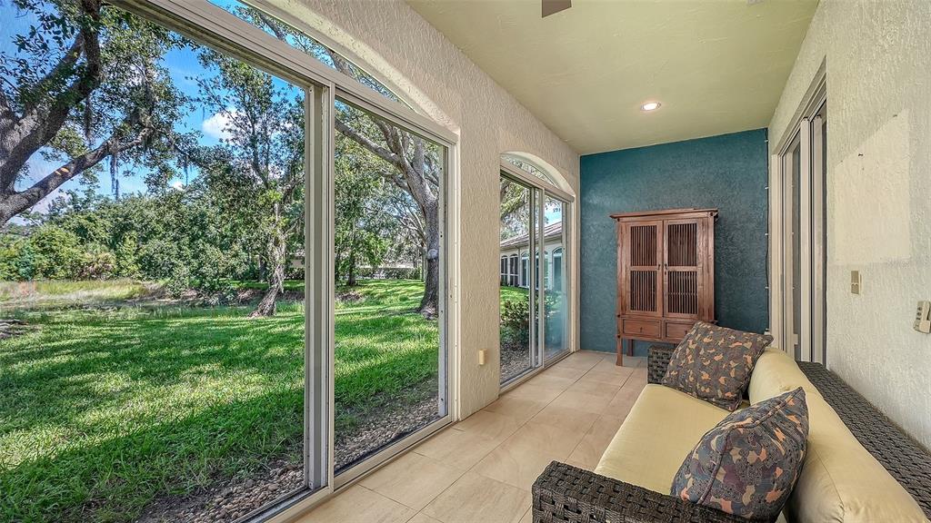 A screened-in porch features tile flooring, a sofa, a wooden cabinet, and views of trees — 3331 HADFIELD GREENE UNIT 49, SARASOTA, FL