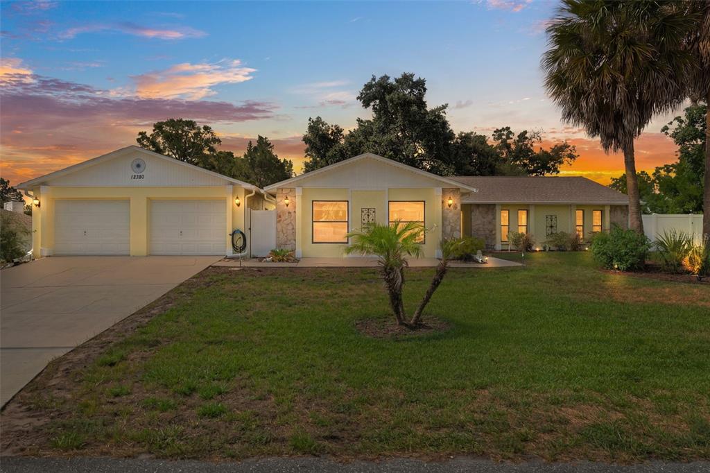 A single-story yellow house with a two-car garage and a front lawn at sunset — 12380 TROUT CIRCLE, SPRING HILL, FL