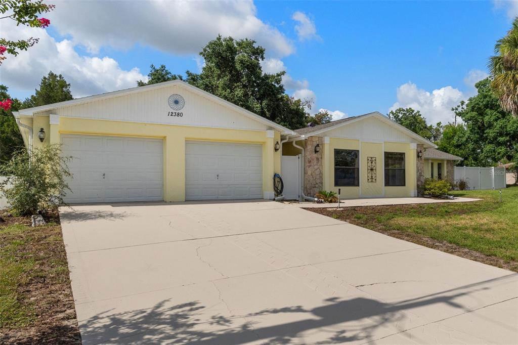 A yellow single-story house with a two-car garage and a concrete driveway — 12380 TROUT CIRCLE, SPRING HILL, FL