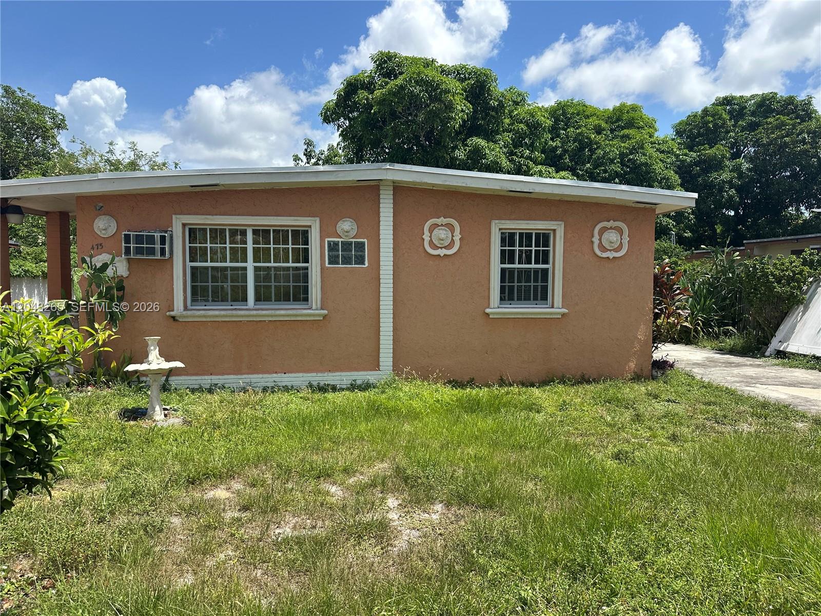 A peach-colored, single-story house features a flat roof, white trim, and decorative wall medallions — NORTH MIAMI, FL