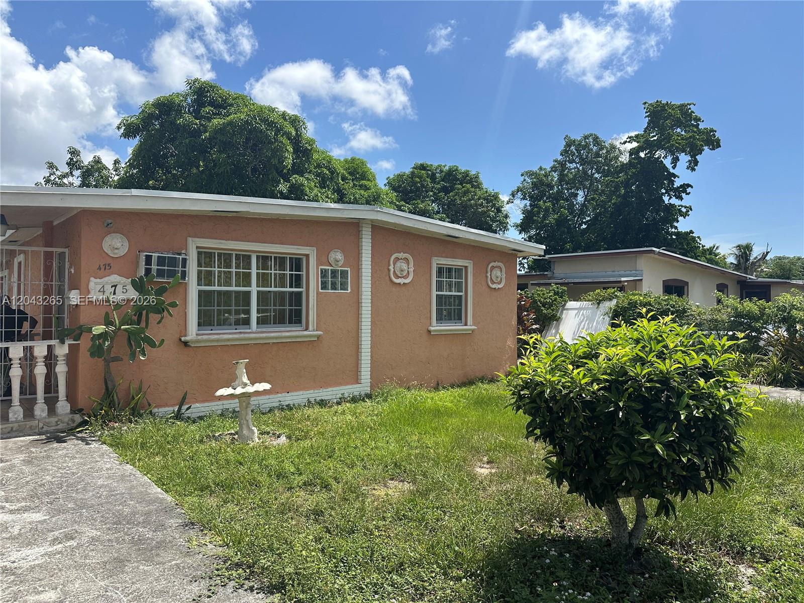 A peach-colored single-story house features a front lawn, a small fountain, and decorative wall accents — NORTH MIAMI, FL