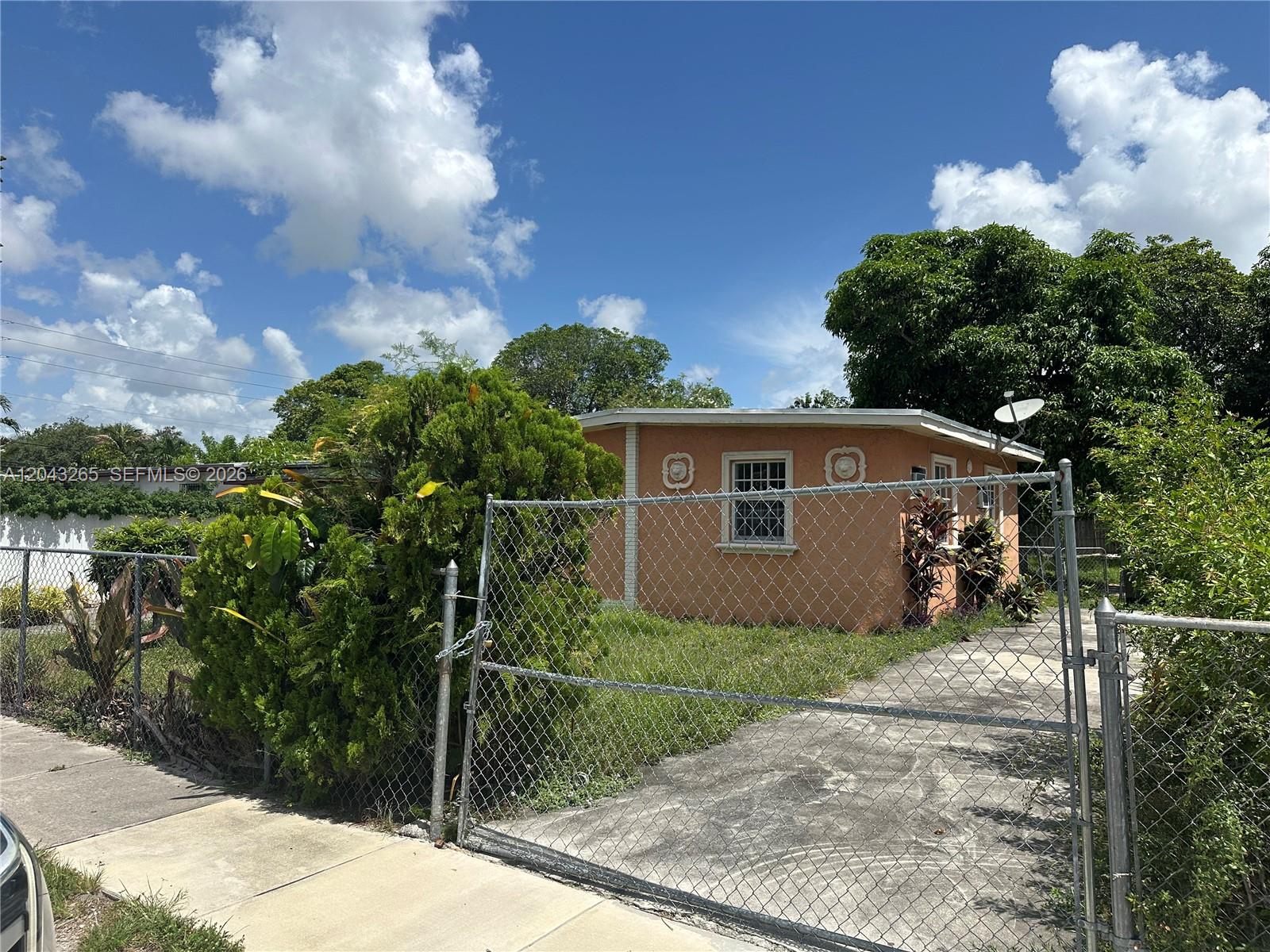 A peach-colored, single-story house is viewed from behind a chain-link fence and gate — NORTH MIAMI, FL