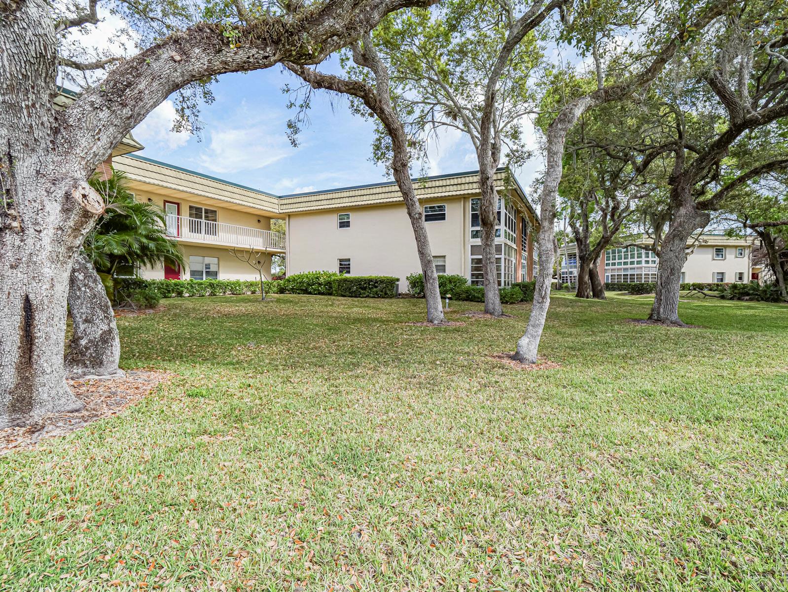A grassy lawn sits in front of a two-story apartment building with mature trees — VERO BEACH, FL