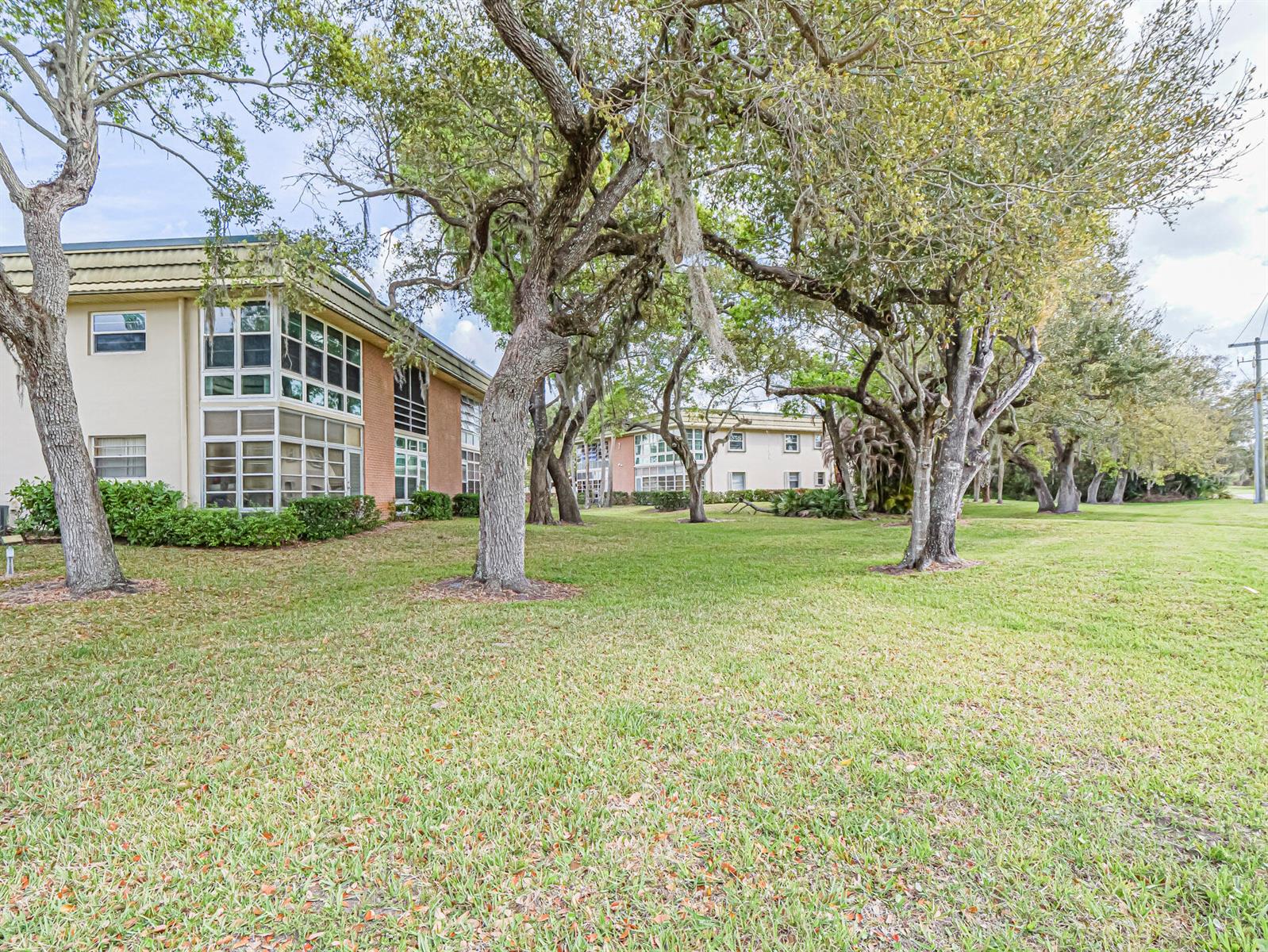 A multi-story apartment building sits behind a grassy lawn with several large, mature trees — VERO BEACH, FL