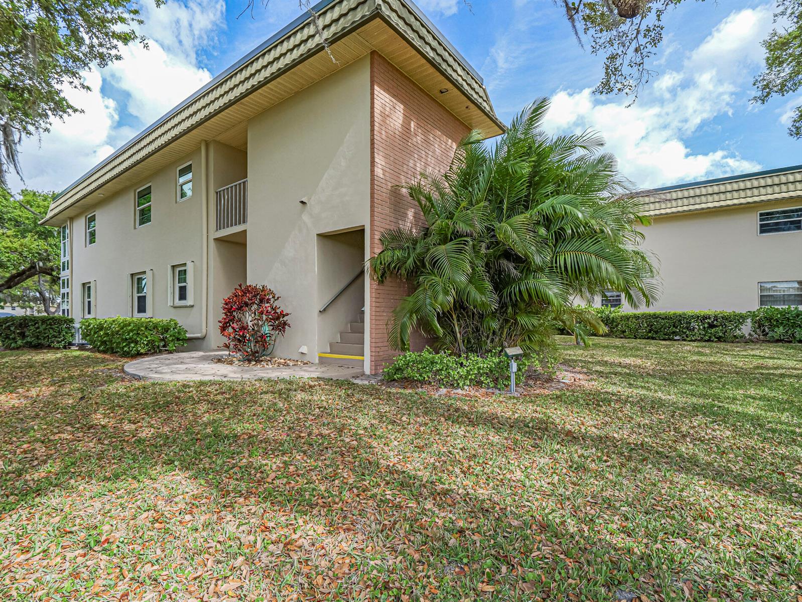 A two-story apartment building exterior features a brick accent wall, stairs, and a palm tree — VERO BEACH, FL
